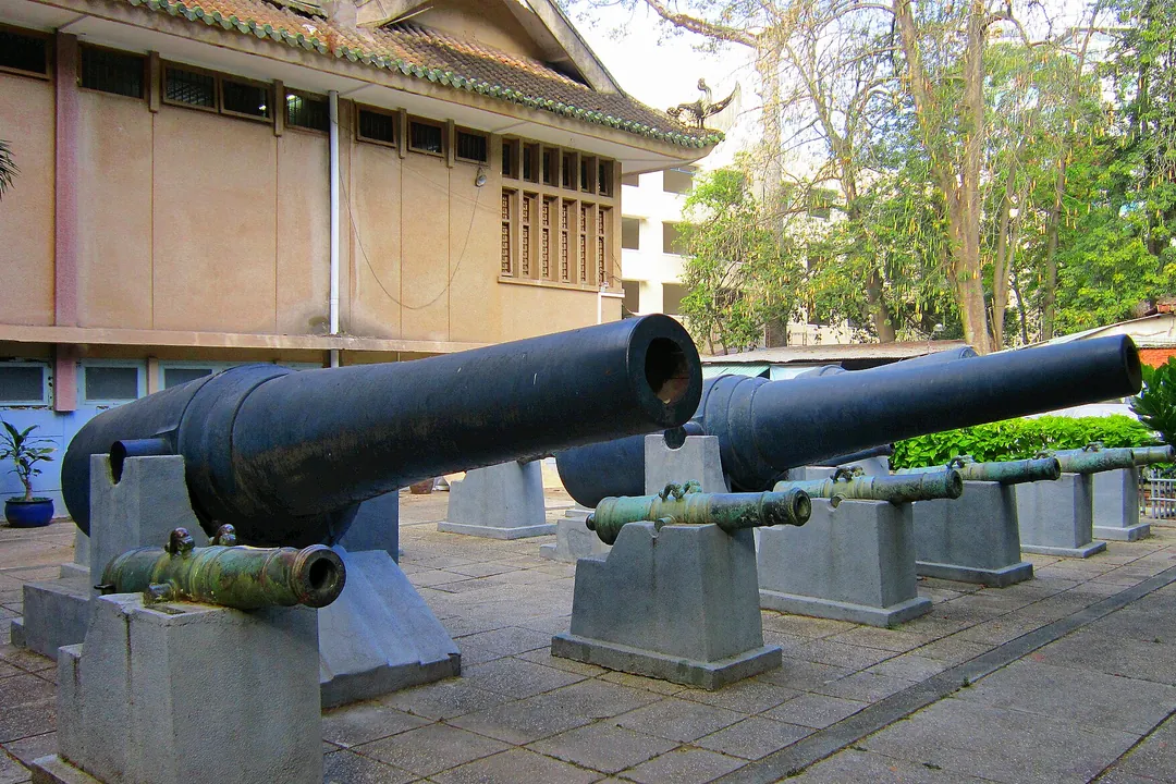 Two large black cannons and a row of small bronze cannons on stone stands outside the museum