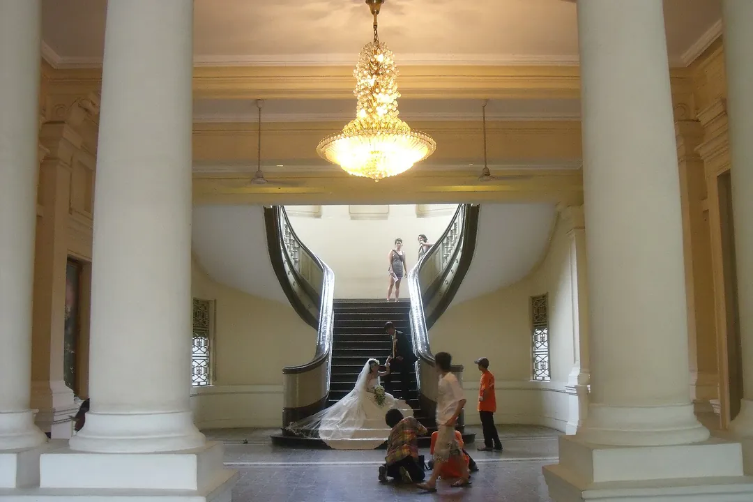 A bride in a long white dress posing on a curved double staircase under a chandelier