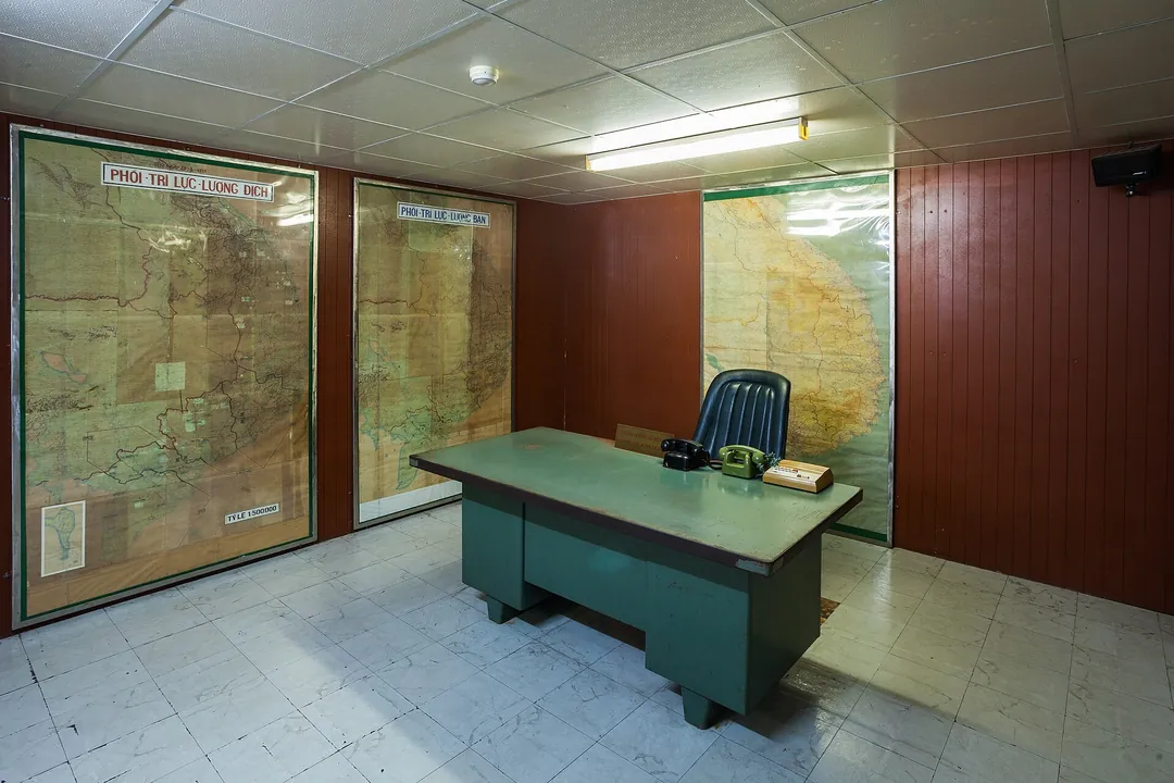 A green metal desk in front of large wall maps in a wood-panelled room