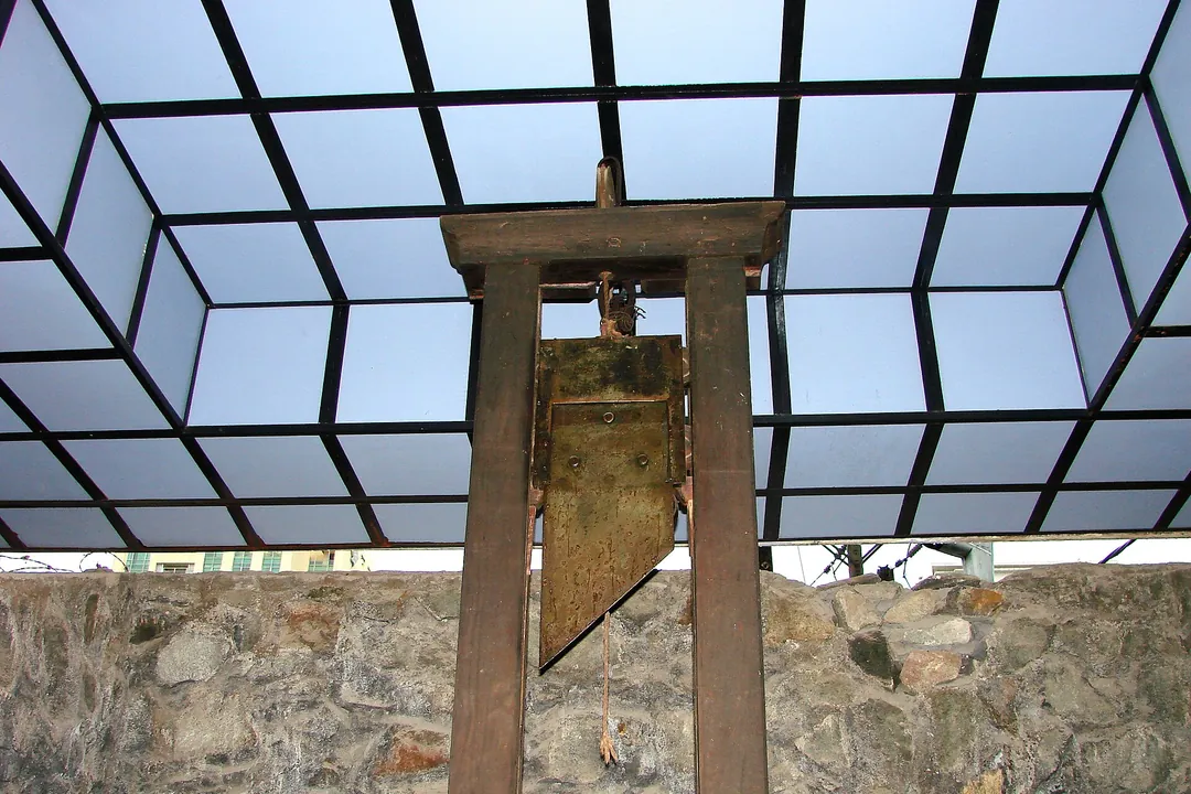 A wooden guillotine under a glass roof in front of a stone wall