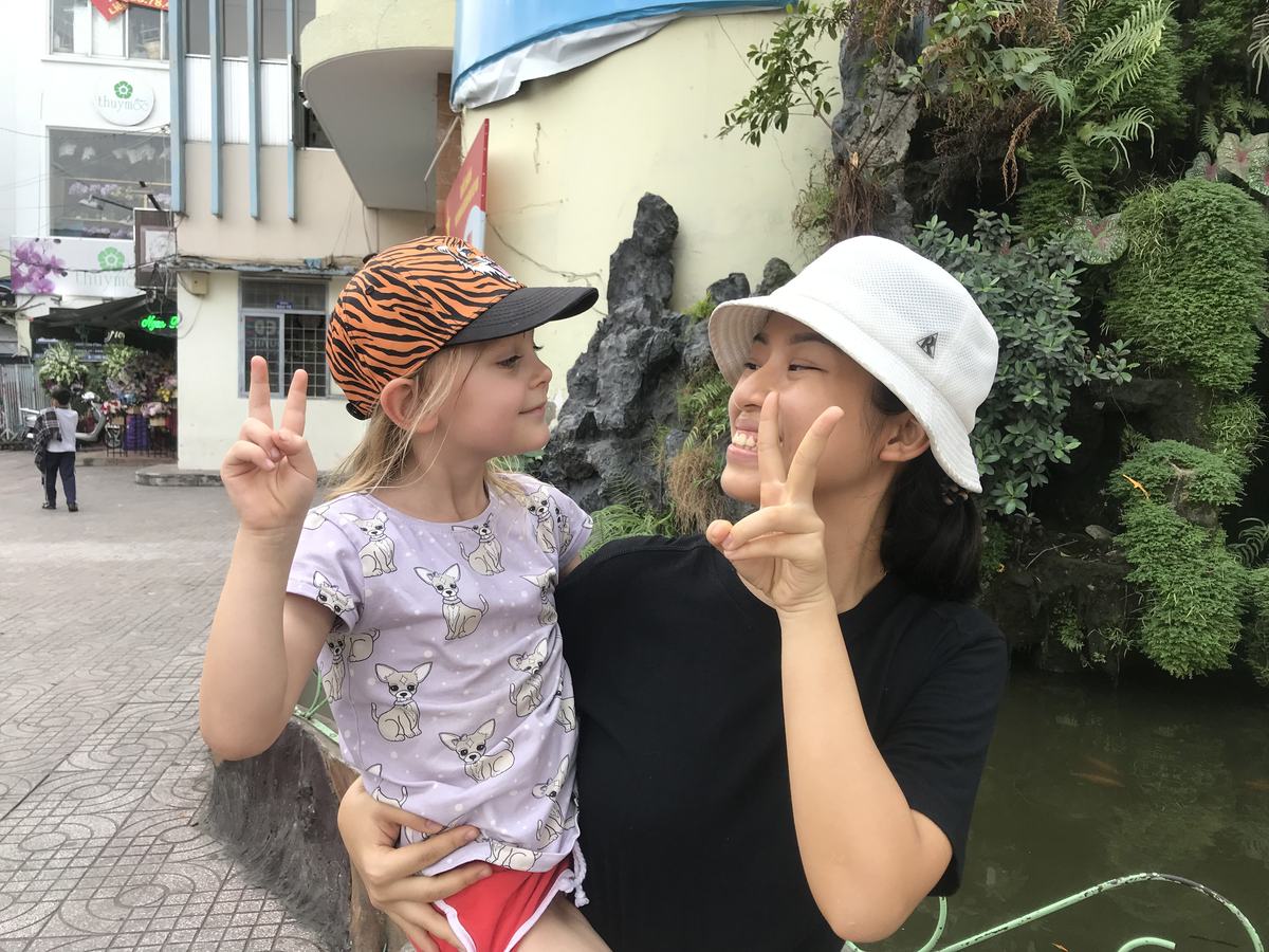 Our guide holding a guest's young daughter by a rock garden and fish pond in Saigon, both making peace signs