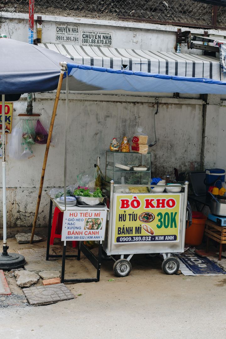 A street cart selling bò kho, hủ tiếu and bánh mì for 30K, with a sign for hủ tiếu mì and bánh canh beside it