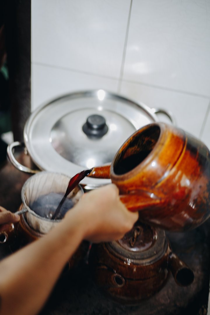 Coffee poured from a glazed clay pot through a cloth sock filter, the old way, beside a big steel pot