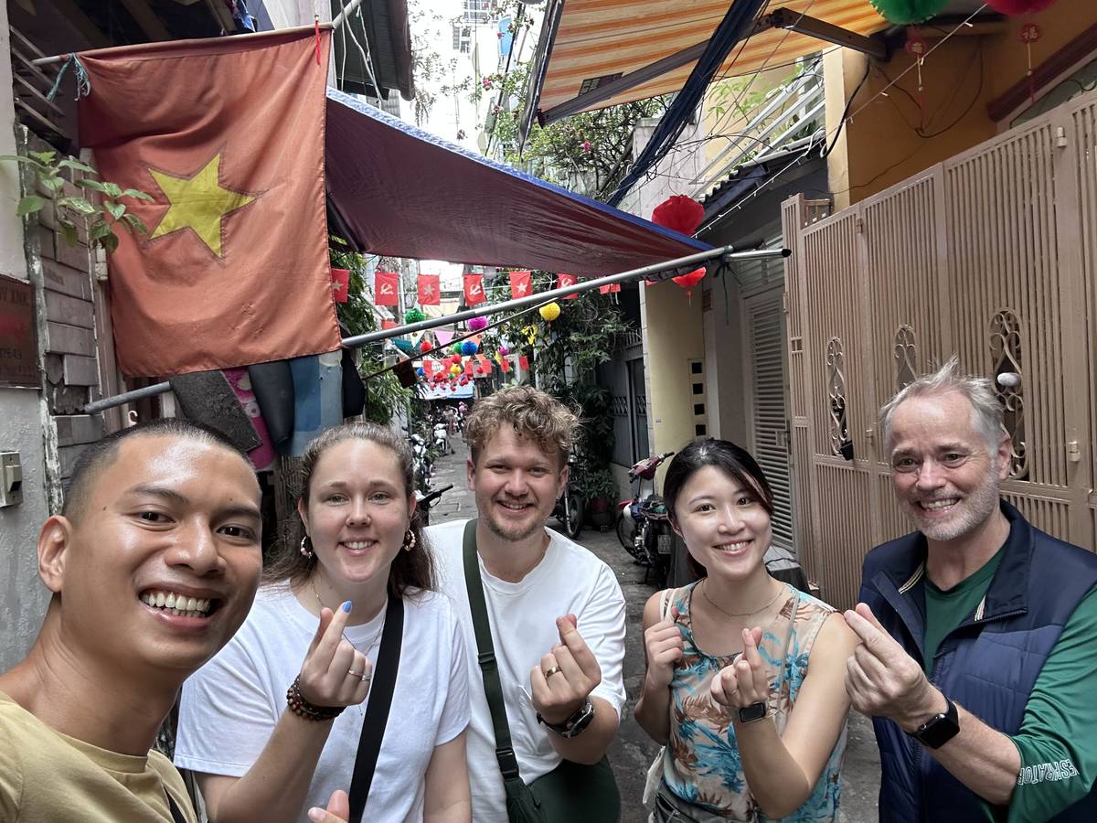 Hieu taking a selfie with four guests making finger hearts in an alley hung with a Vietnamese flag and strings of small red flags