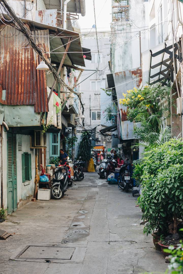 A quiet hẻm in the morning: rusty tin roofs, potted plants and motorbikes parked along both sides