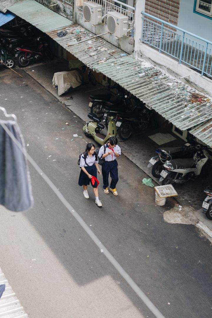 Two schoolgirls in white shirts and red Young Pioneer scarves walking down a lane in the morning, seen from a balcony above