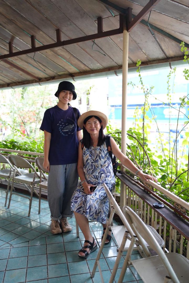Spring and a guest in a straw hat standing on a covered balcony with tiled floor and plants growing along the railing