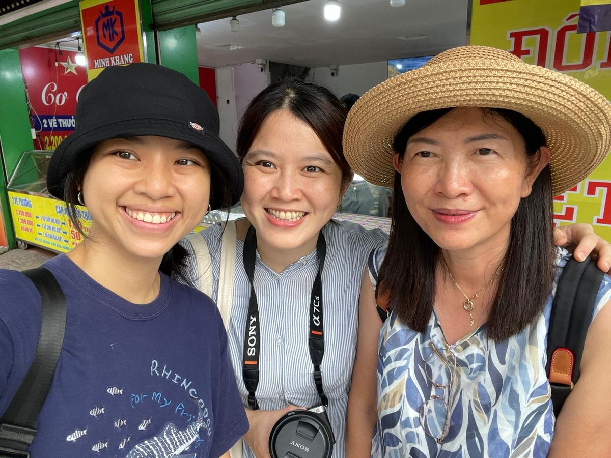 Spring in a black bucket hat taking a selfie with two guests outside a shop, one guest in a straw hat and one with a camera round her neck