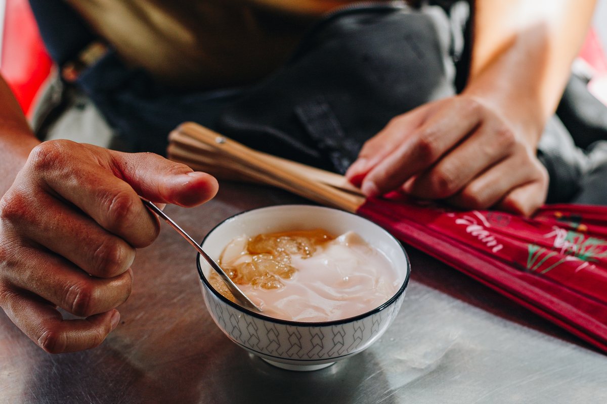 One of our team with a bowl of tàu hũ, silken tofu in syrup, holding a red folding fan