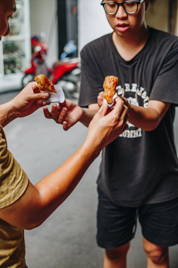 Two of our team tearing open chuối chiên, banana fritters in paper wraps, on the street