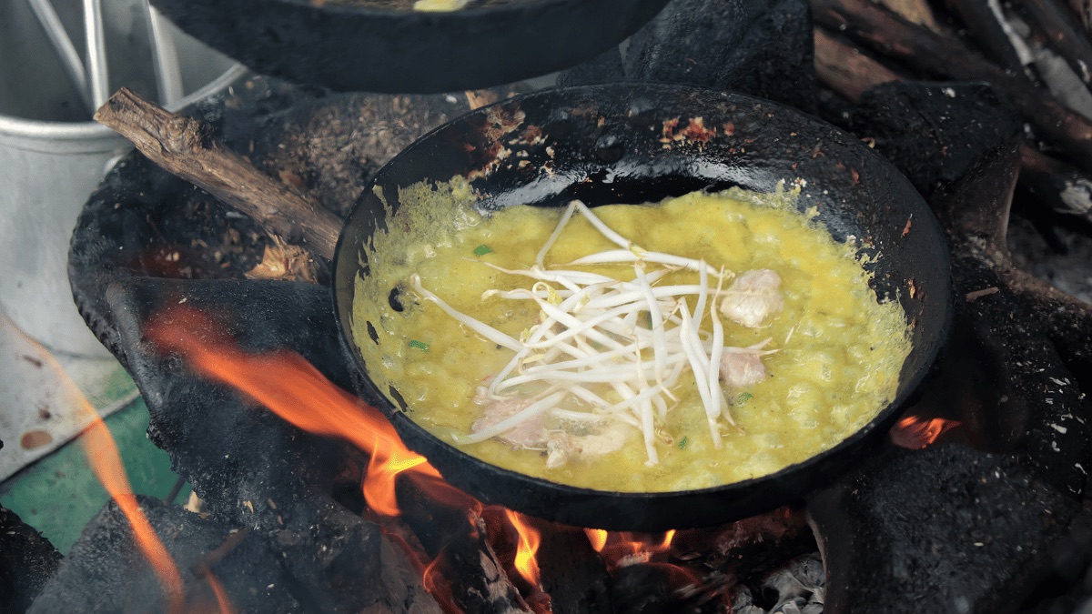 A wok of food cooking over an open flame during a home cooking class