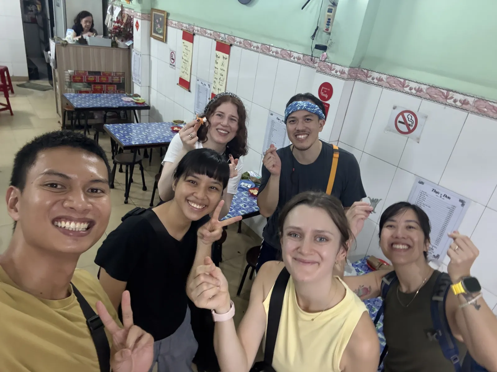 Hieu taking a selfie with five guests in a small tiled eatery, the guests holding up bites of food