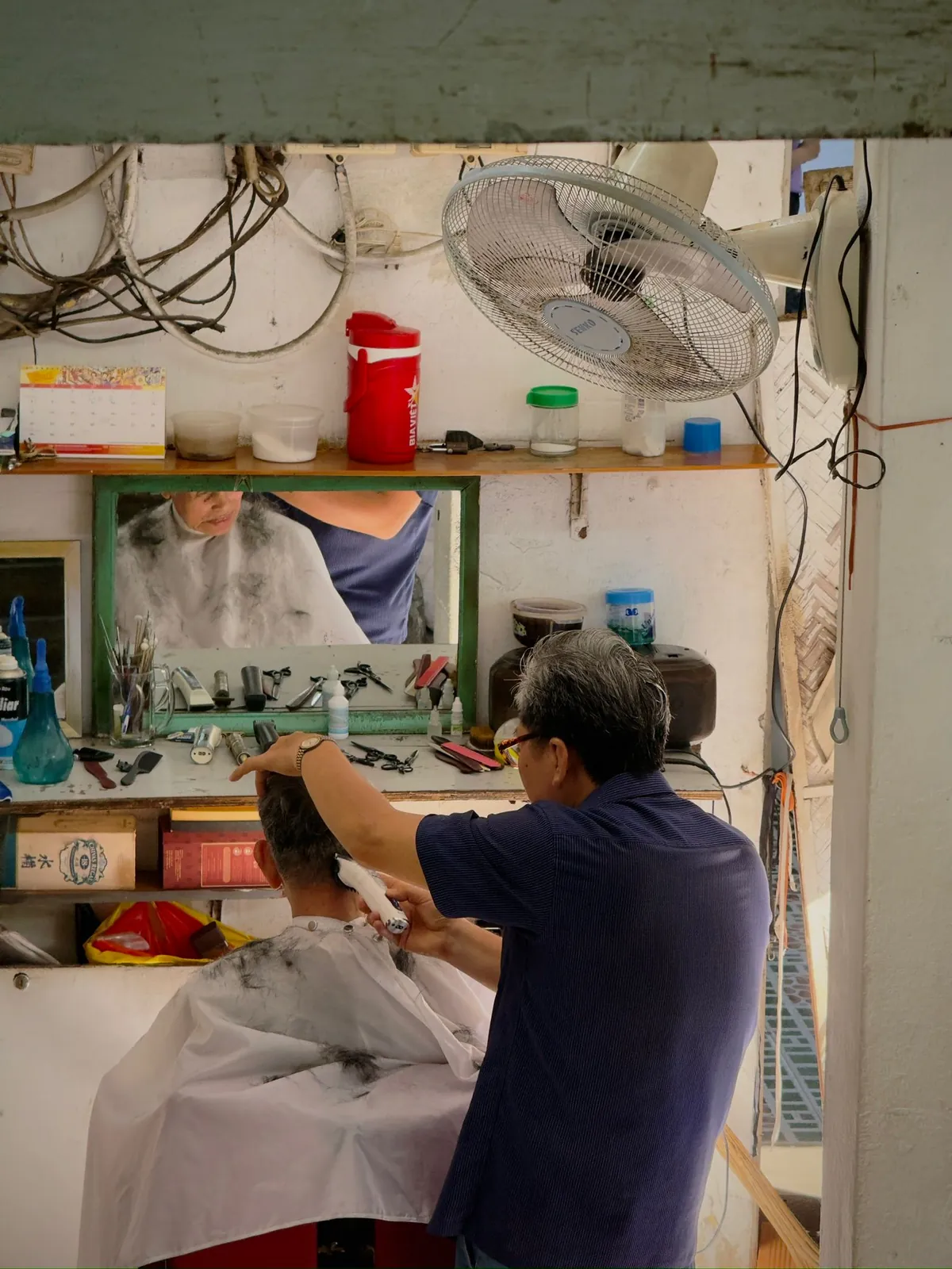 A barber cutting a customer's hair at a small street barbershop
