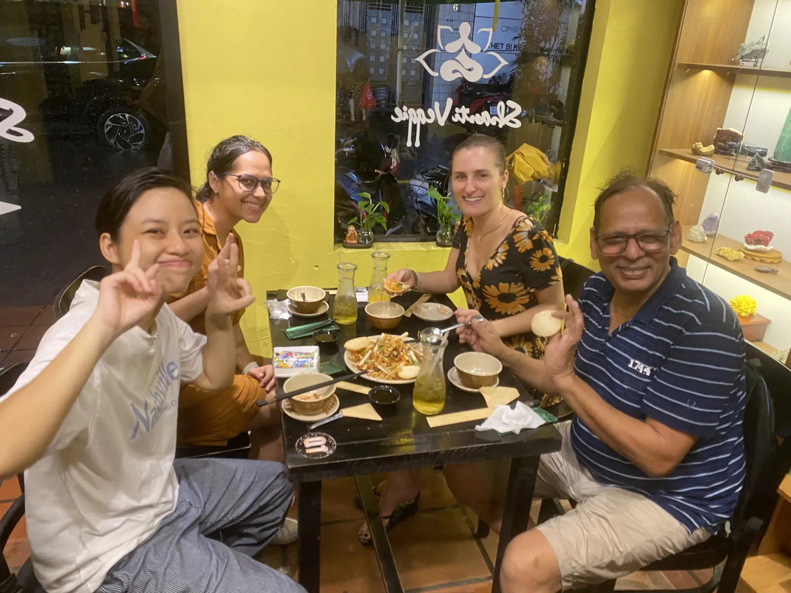 Four guests laughing over a vegan dinner spread at a yellow restaurant