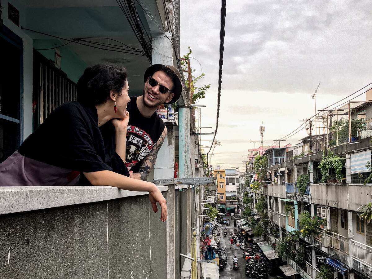 Two guests leaning on a walkway wall high up in the 1968 Nguyen Thien Thuat apartment blocks, the street and old blocks stretching away below