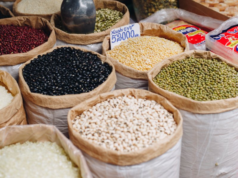 Open sacks of black beans, mung beans, peanuts and rice at a market stall, with a handwritten price sign