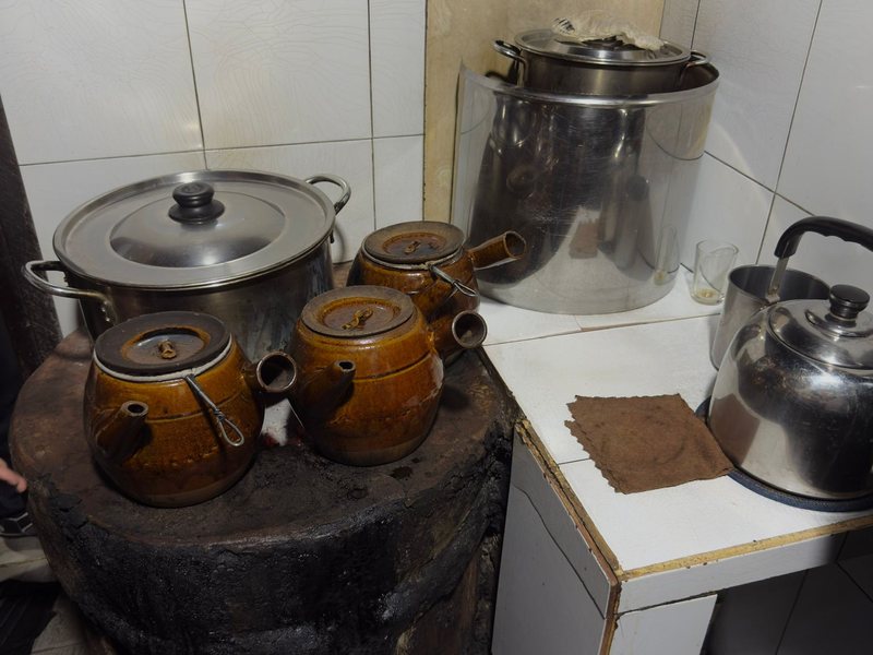 Glazed clay coffee pots on a soot-blackened charcoal stove at Cheo Leo cafe, a cloth filter drying beside them