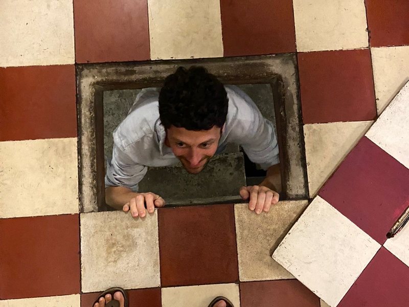 A guest climbing up out of the hatch to the hidden weapons bunker, set in the red and white floor tiles