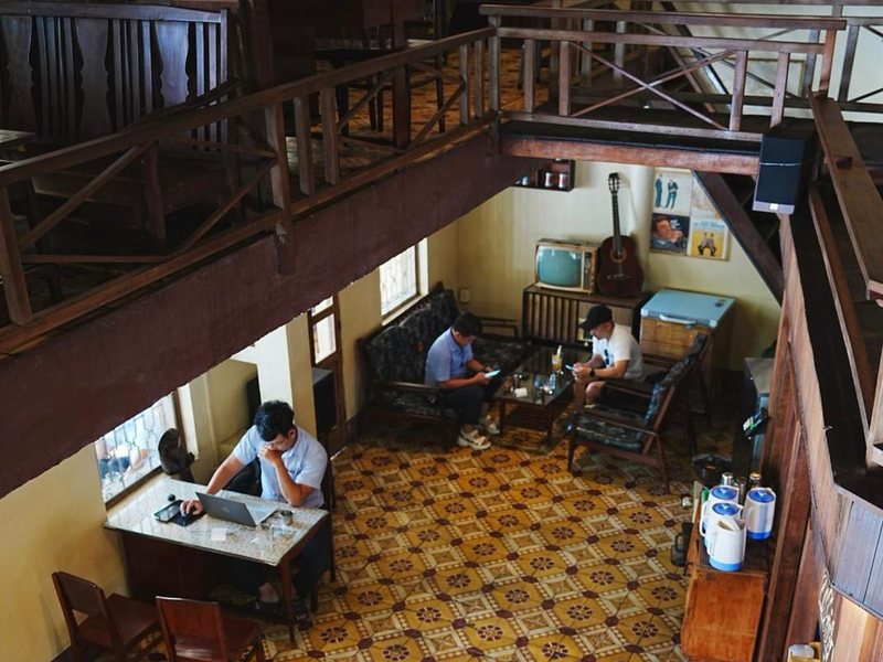 The old cafe seen from its wooden mezzanine: patterned tile floor, a few people at tables and sofas below