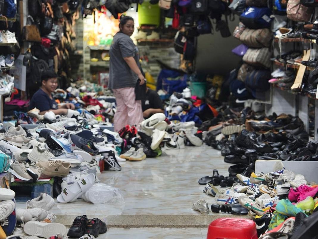 A shoe stall with sneakers and sandals piled across the floor and bags hanging from the ceiling