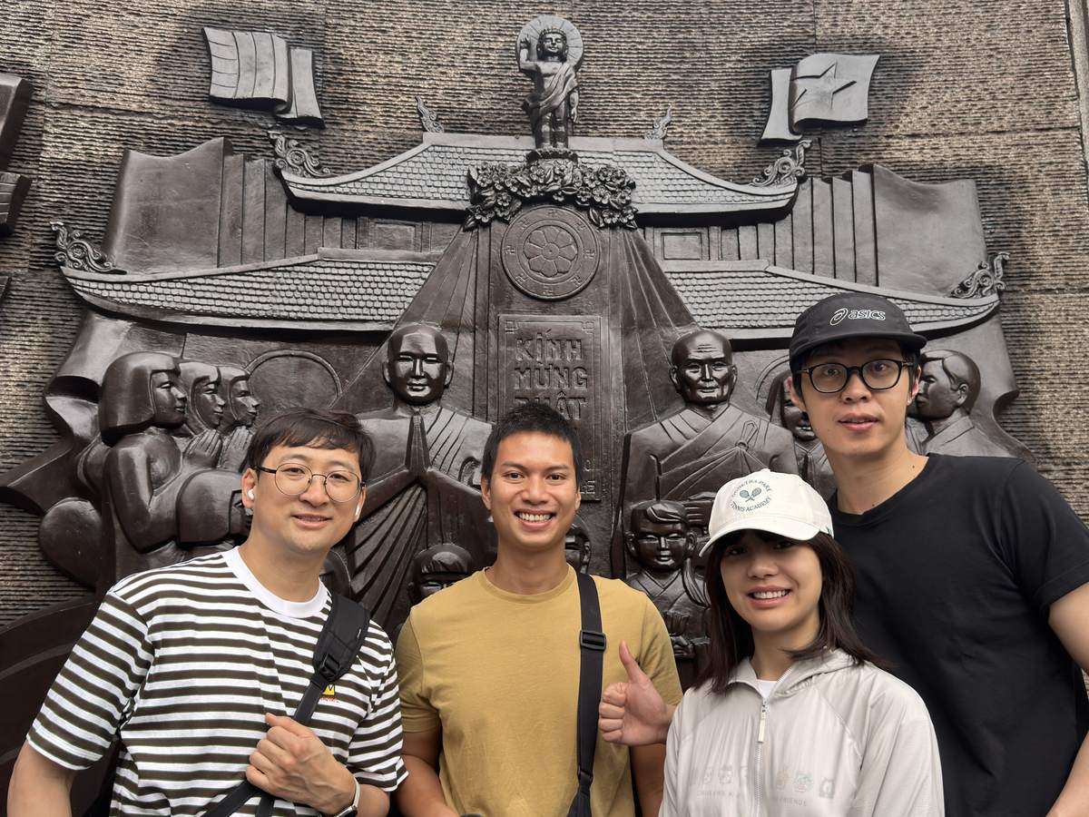 Hieu with three guests in front of the bronze relief of monks and a pagoda at the Thich Quang Duc memorial