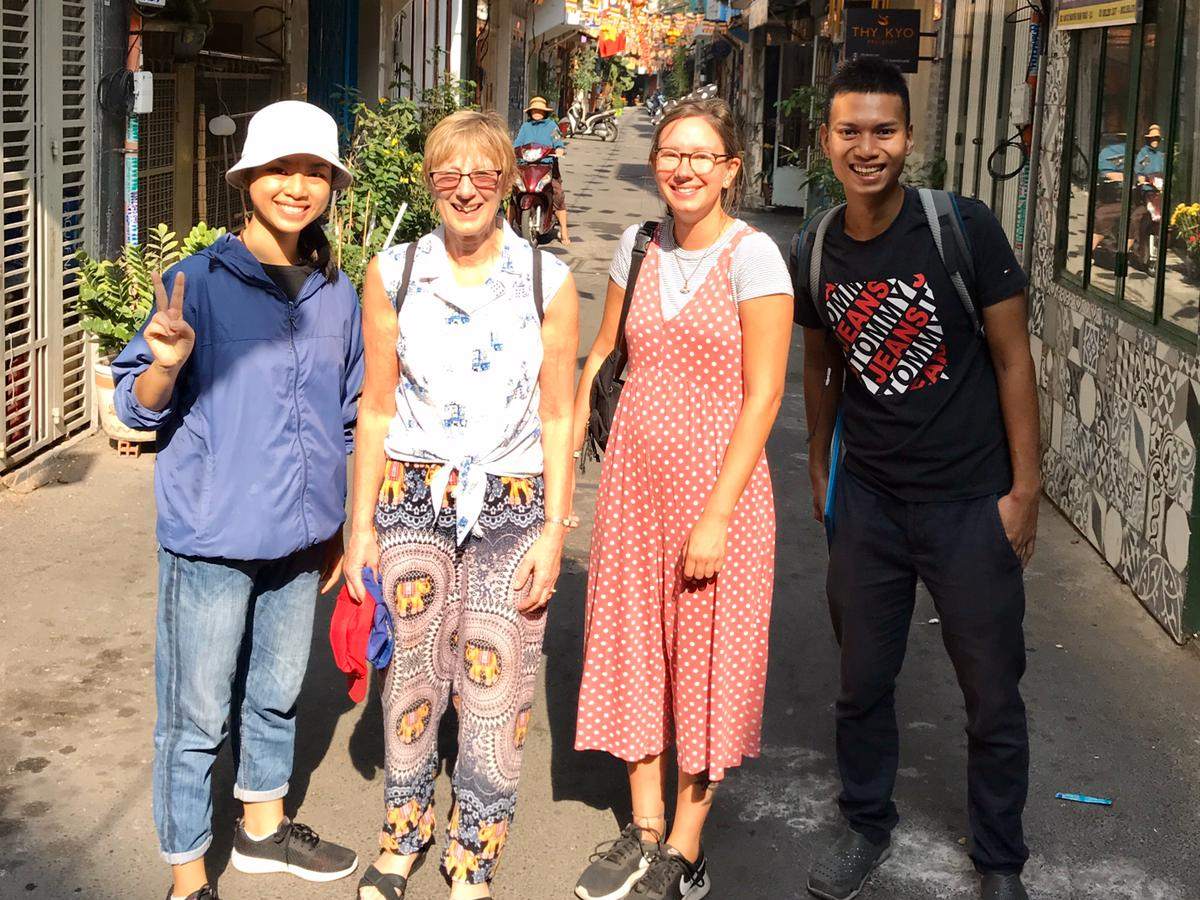 A small tour group standing in a sunny alley strung with Buddhist flags