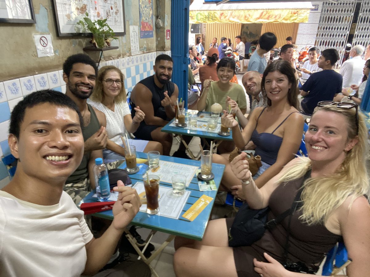 Hieu taking a selfie with six guests over iced coffee at Cheo Leo cafe, the lane busy behind them