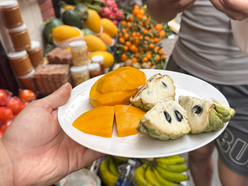 A plate of cut mango and custard apple held up at a fruit stall