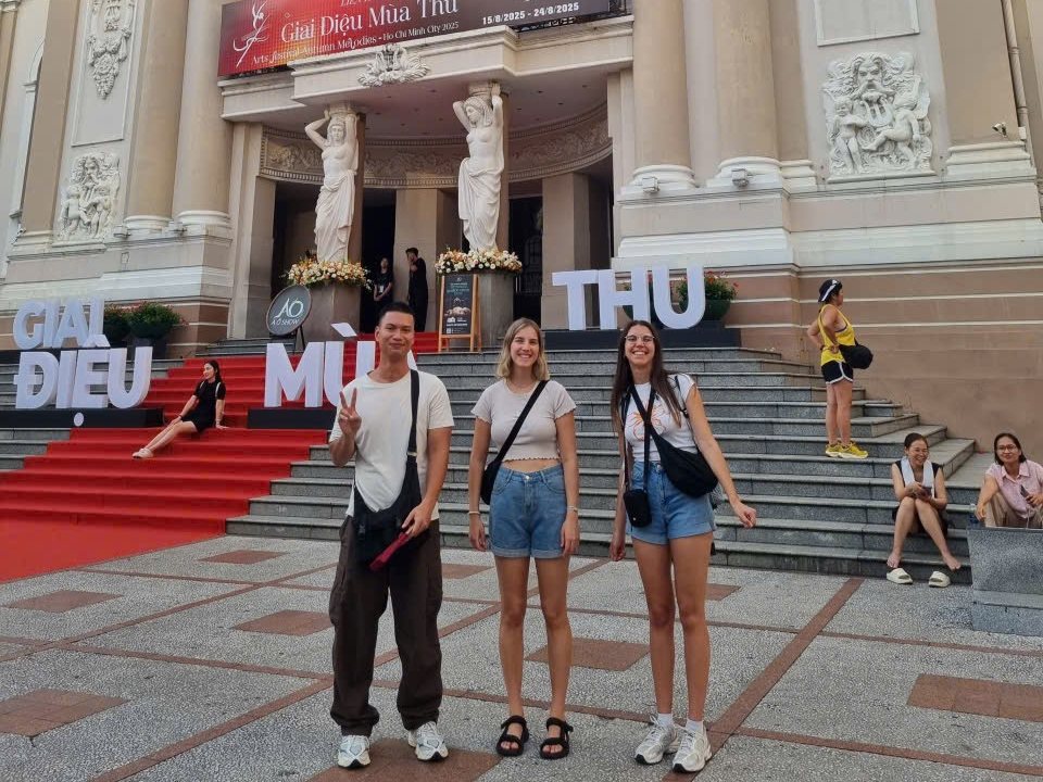 Guests on the forecourt of the Saigon Opera House in the daytime, its carved front and steps behind them