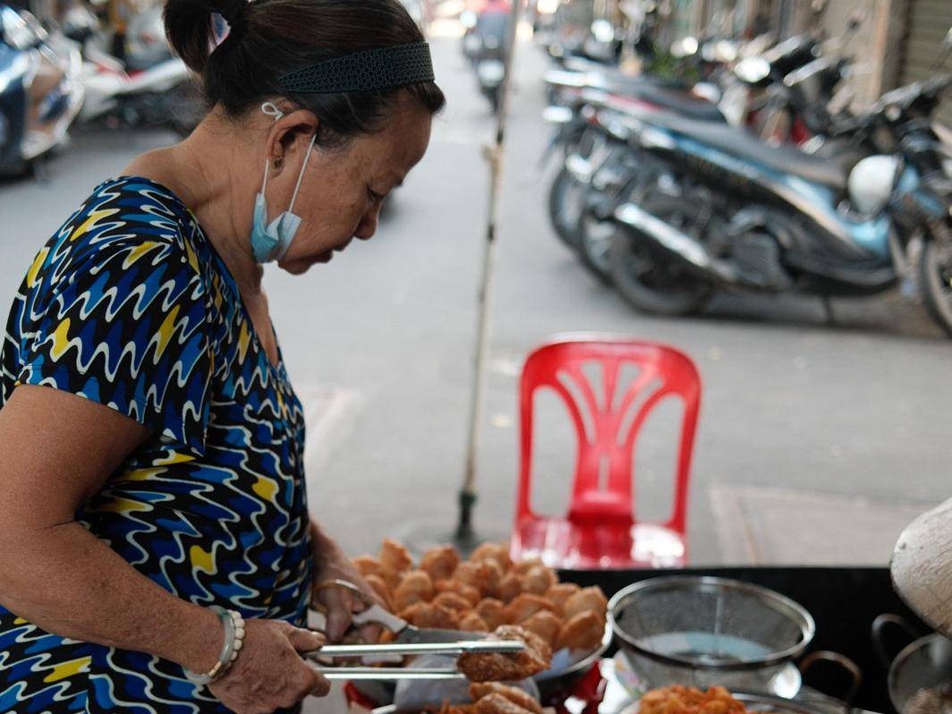 A street vendor frying snacks at her stall, scooters parked behind her