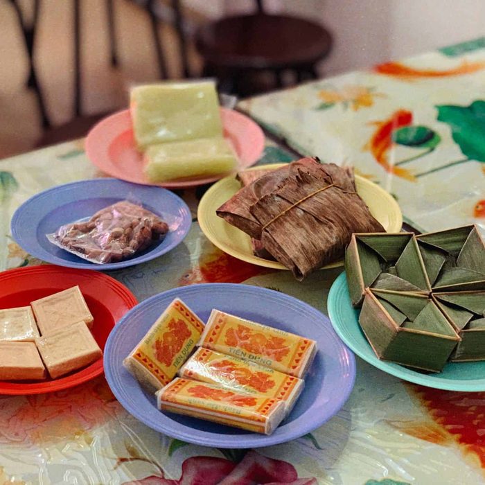 Plates of traditional cakes on a flowered tablecloth: mung bean cakes, leaf-wrapped rice cakes and green rice cakes
