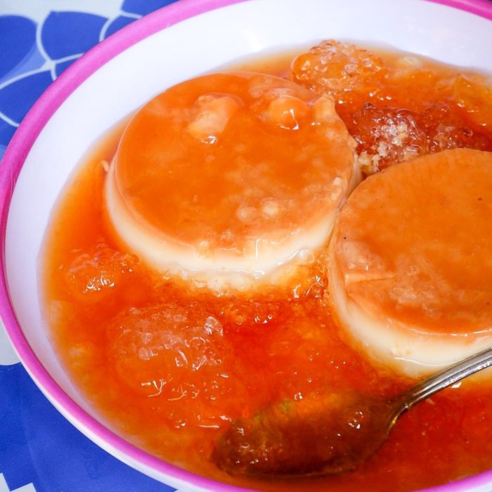 Two rounds of bánh flan in a pink-rimmed bowl under orange syrup and crushed ice