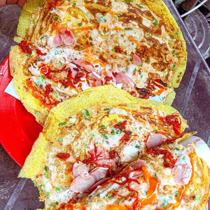Two pieces of bánh tráng nướng covered in egg, sliced sausage, spring onion, chilli sauce and mayonnaise