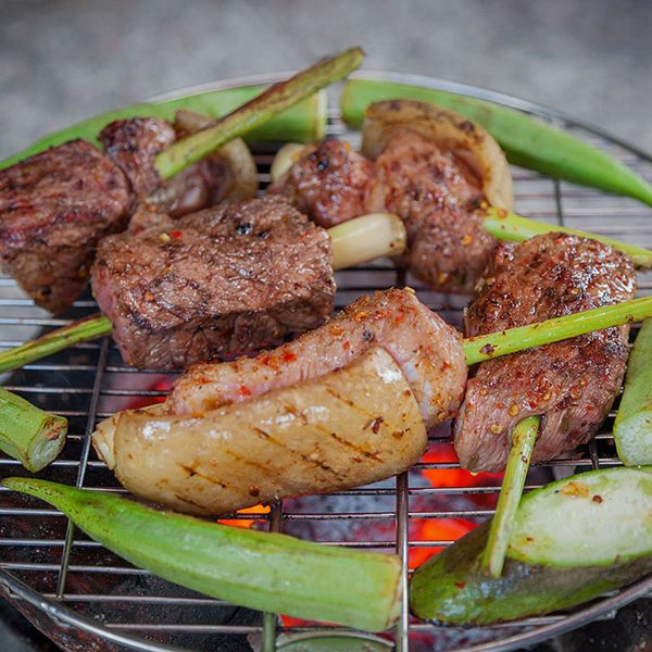 Bê nướng lụi sả: chunks of veal on lemongrass stalks grilling over charcoal with okra