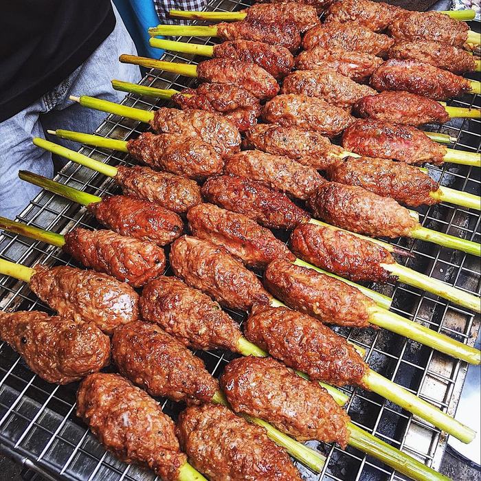 Rows of bò lụi sả on a wire grill: minced beef pressed around lemongrass stalks and browned all over
