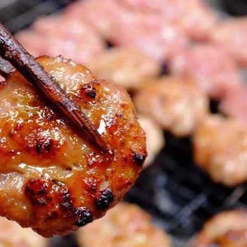 A grilled pork patty held up with chopsticks over more patties on a charcoal grill
