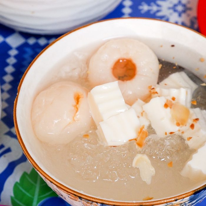 A bowl of chè with peeled lychees and cubes of almond jelly over crushed ice, sprinkled with toasted almond