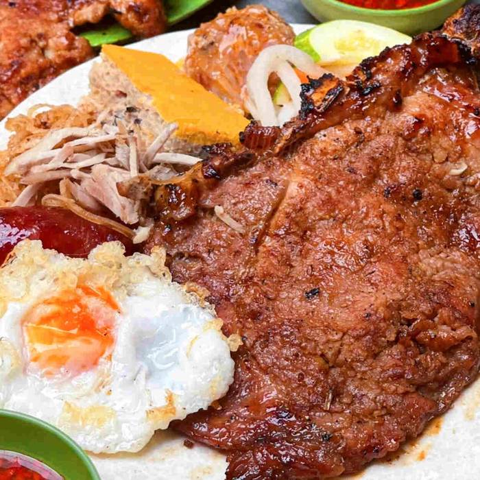 Cơm tấm with a big grilled pork chop, a fried egg, Chinese sausage, shredded pork skin and a slice of egg meatloaf