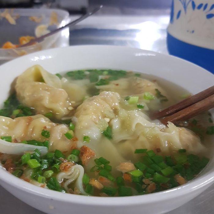 A bowl of hoành thánh, wonton soup, with spring onion and fried shallots, chopsticks resting in it