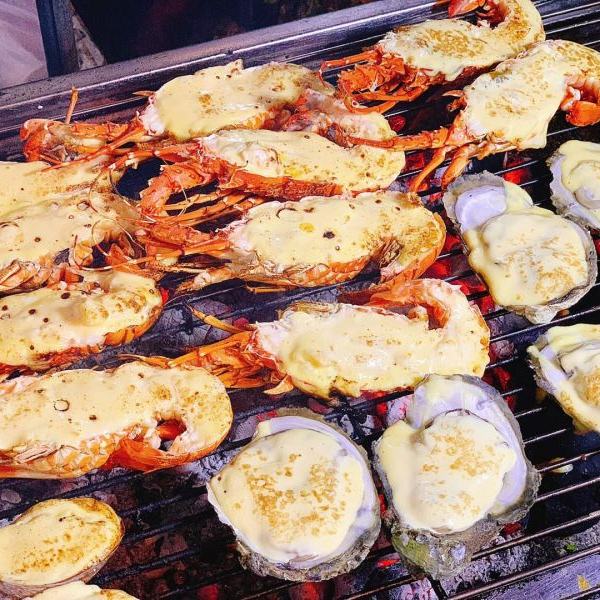 Lobster halves and oysters grilling over charcoal, each topped with melted cheese